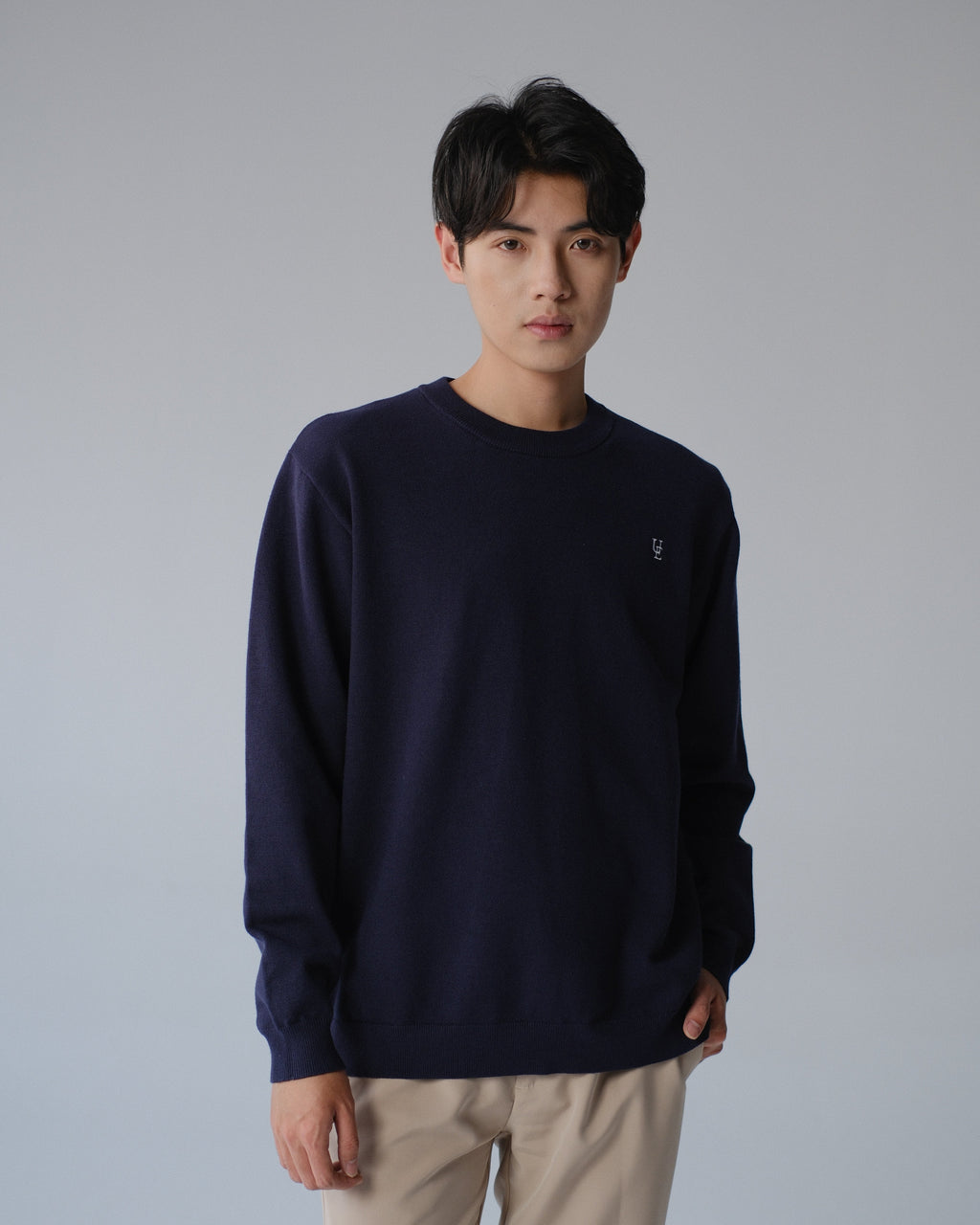 Person wearing a navy sweater and beige pants on a gray background