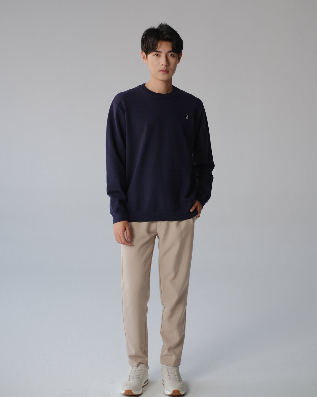 Man wearing a navy sweater and beige pants on a gray background
