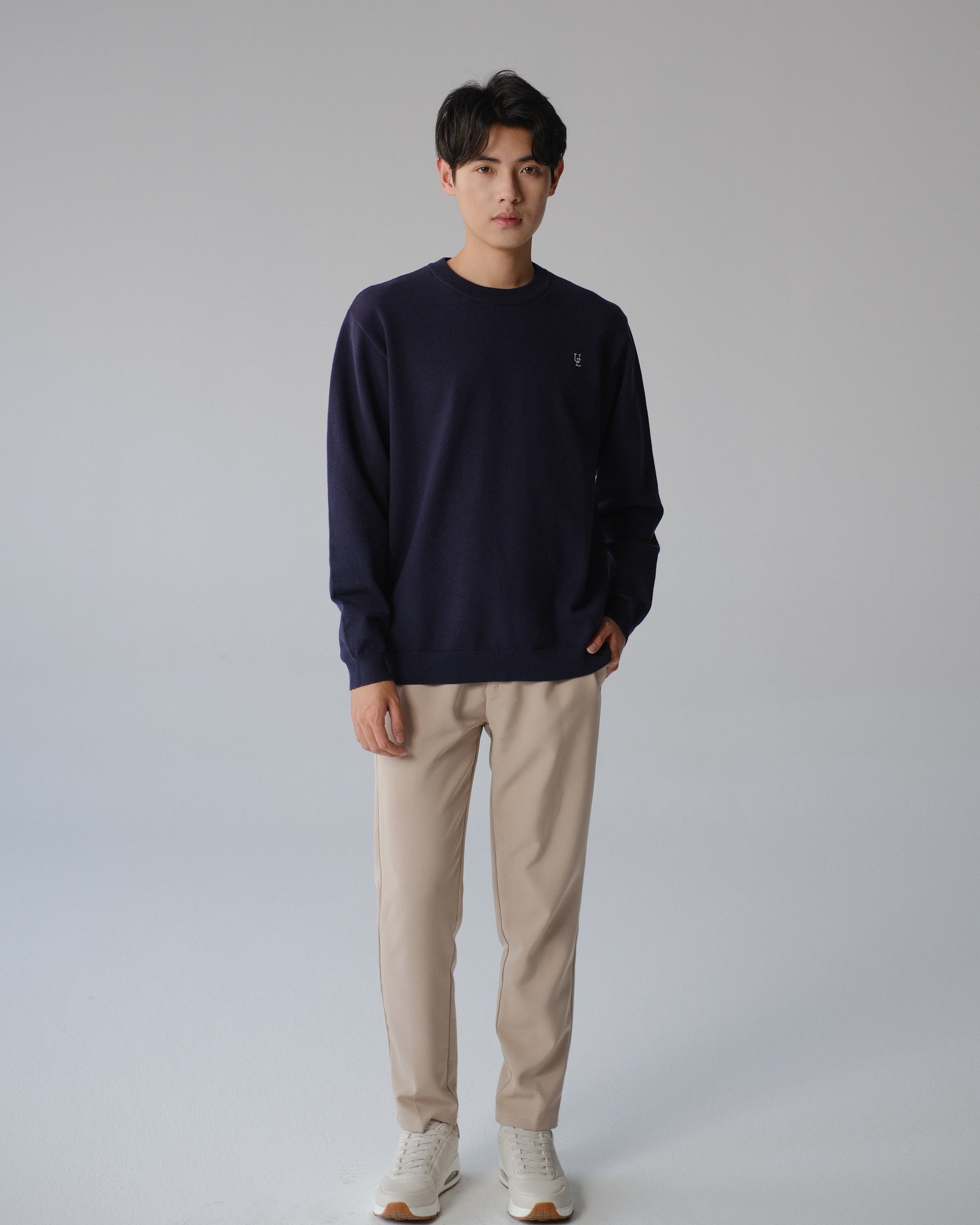 Man wearing a navy sweater and beige pants on a gray background