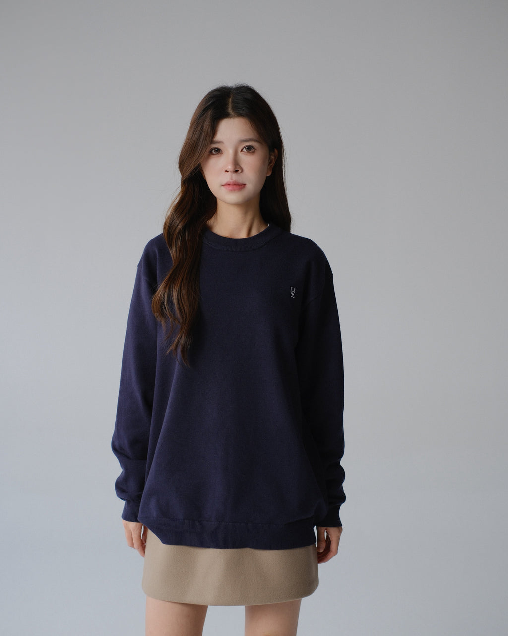 Woman wearing a navy blue sweater and beige skirt on a gray background