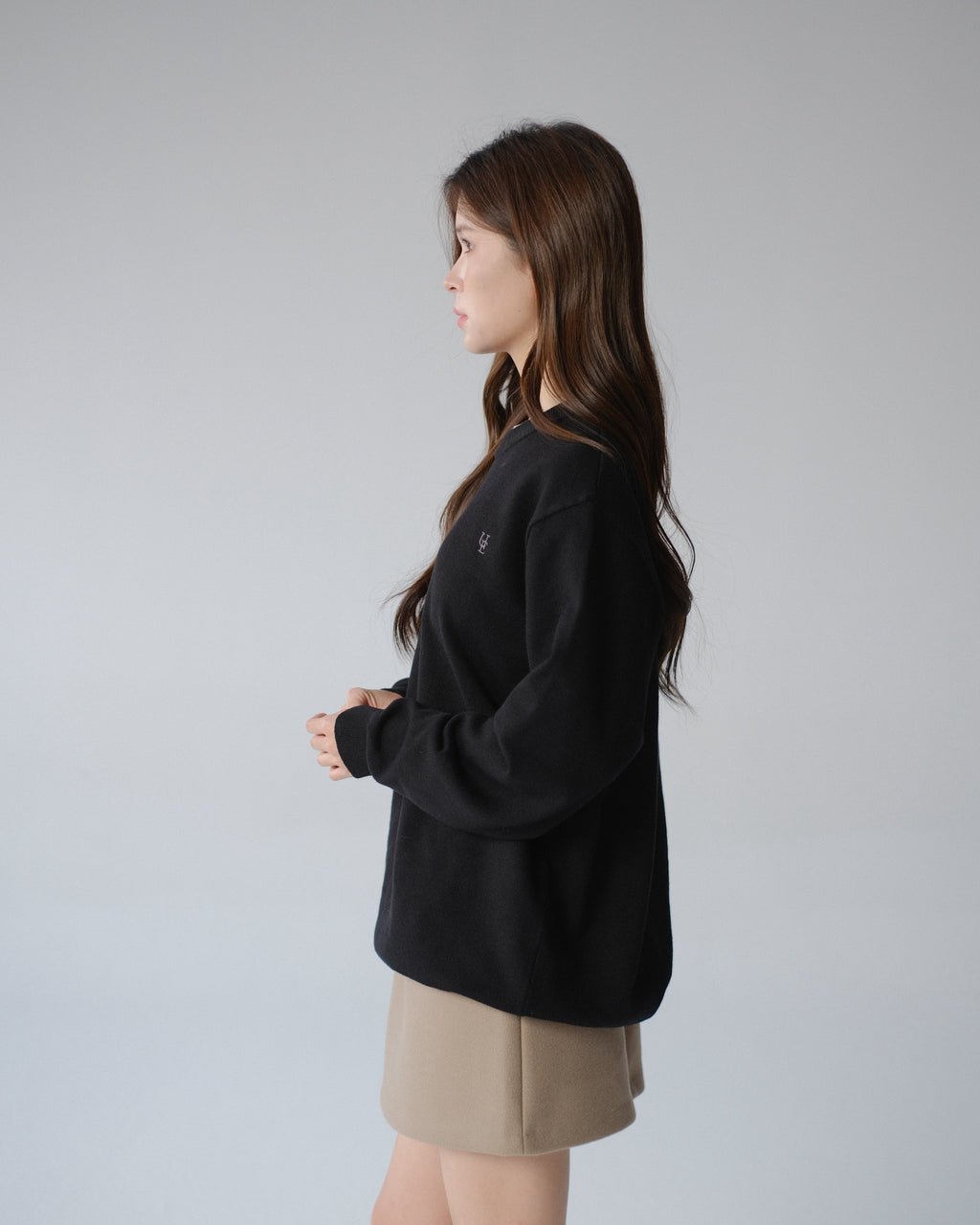 Woman wearing a black sweater and beige shorts against a gray background