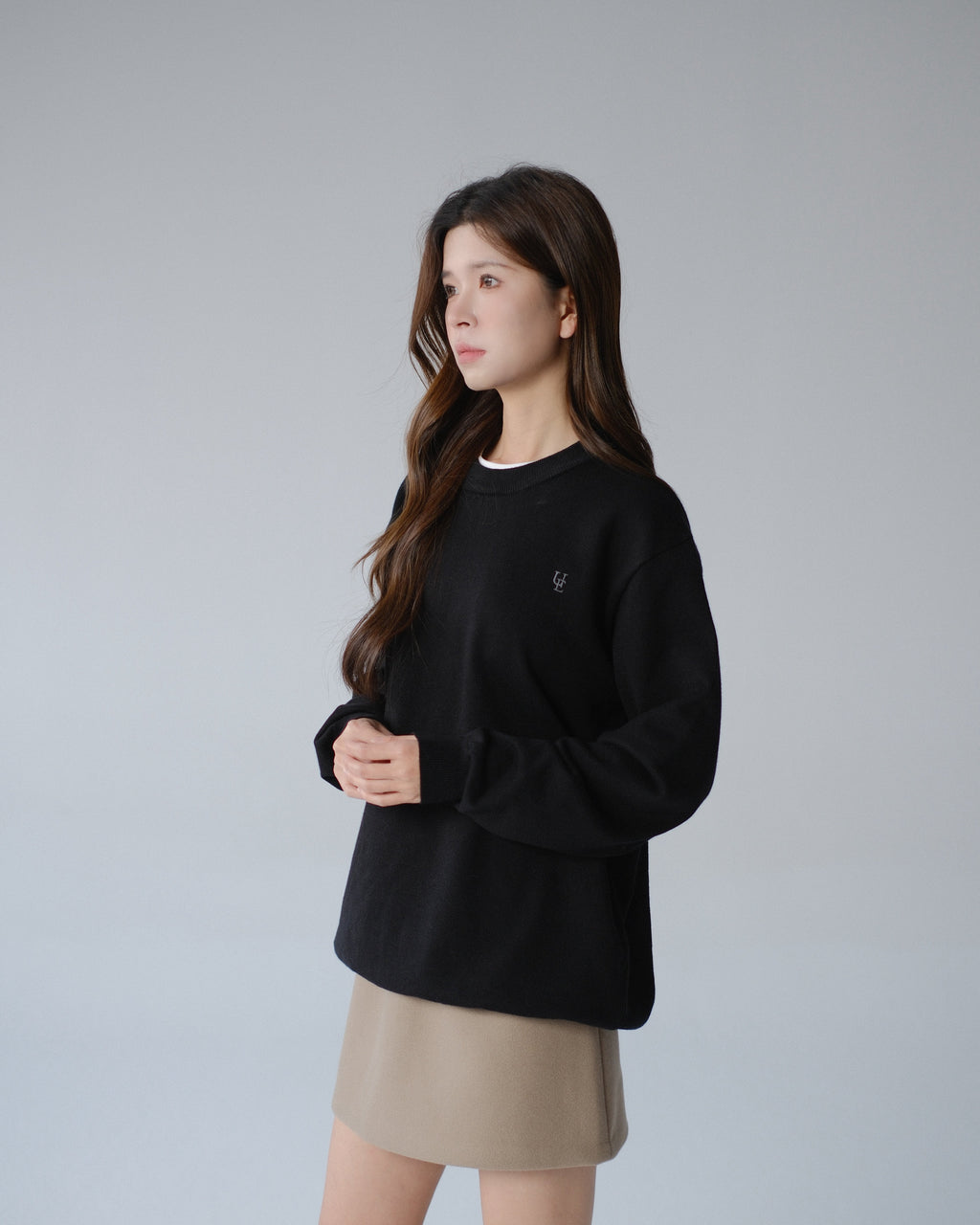 Woman wearing a black sweater and beige skirt on a gray background
