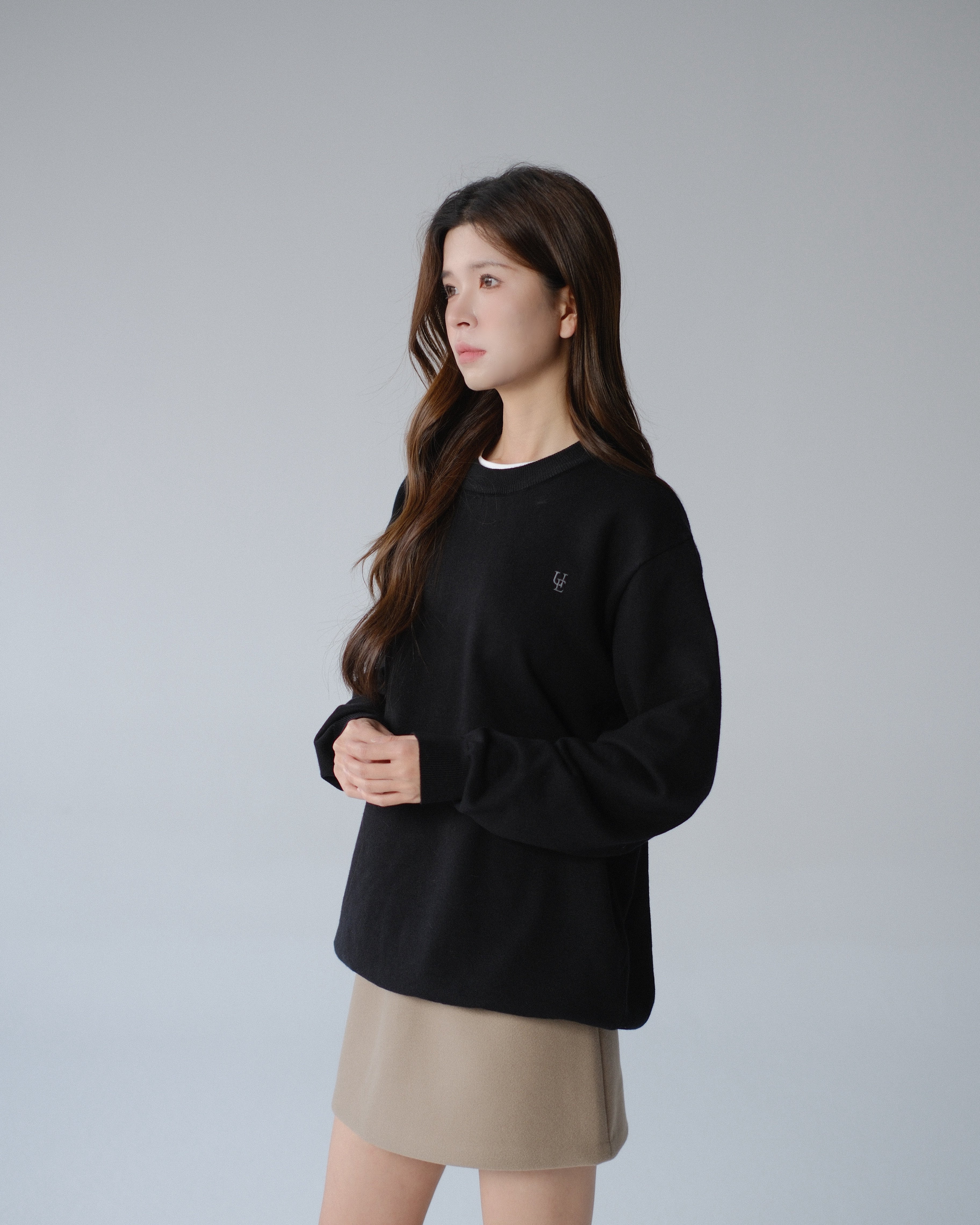Woman wearing a black sweater and beige skirt on a gray background